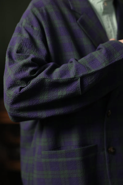Close-up of a person wearing a dark purple plaid shirt with a blurred background
