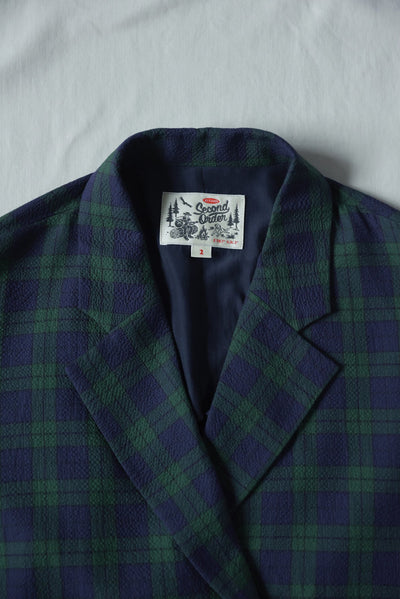 Green and blue plaid jacket with a brand label on a light gray background
