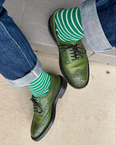 Thick cotton crew socks with green stripe design paired with green leather footwear.